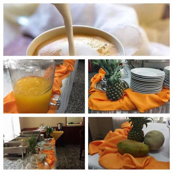 Mesa de buffet con manteles naranjas, piña, fruta, jugo y platos apilados para una comida con servicio de catering.