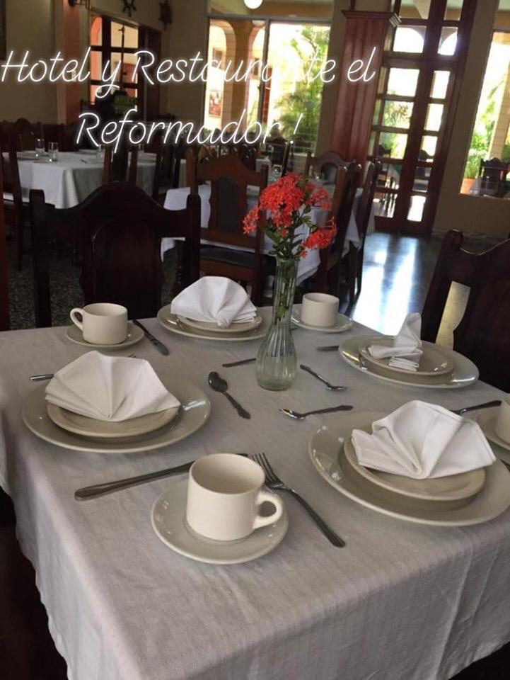 Preparar la mesa del comedor con tazas, servilletas dobladas, platos y flores en el comedor de un restaurante.
