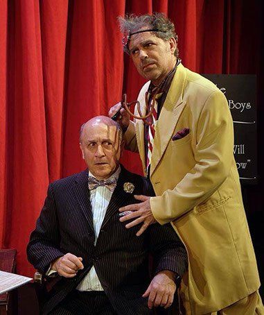 Seated man in black jacket with man in long yellow jacket standing next to him