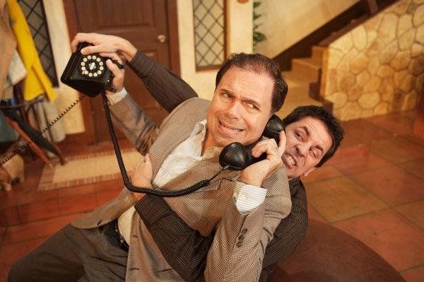 Man in brown jacket talking on phone while other man is pulling him down