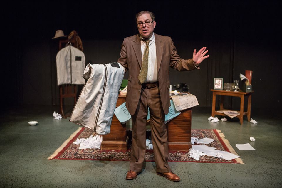 As Bernie standing onstage holding garment bag