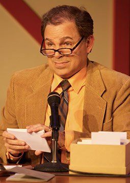 1 actor onstage wearing glasses and holding index cards