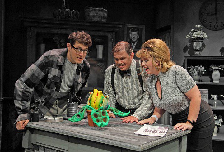 3 actors onstage in costume looking at plant