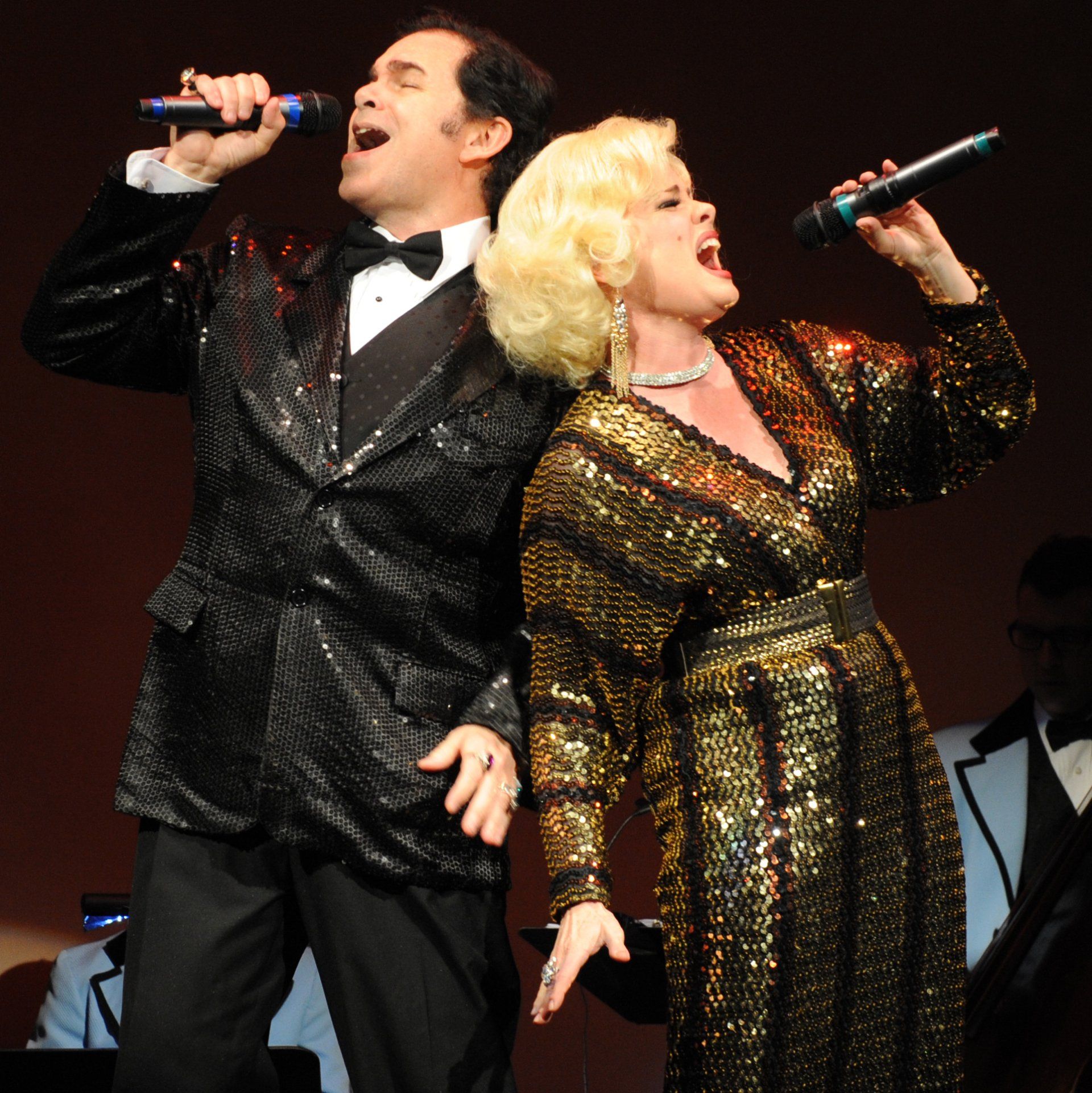 Man in black tux and women in black dress onstage singing