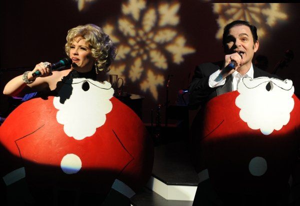 2 actors onstage with Santa props and holding microphones