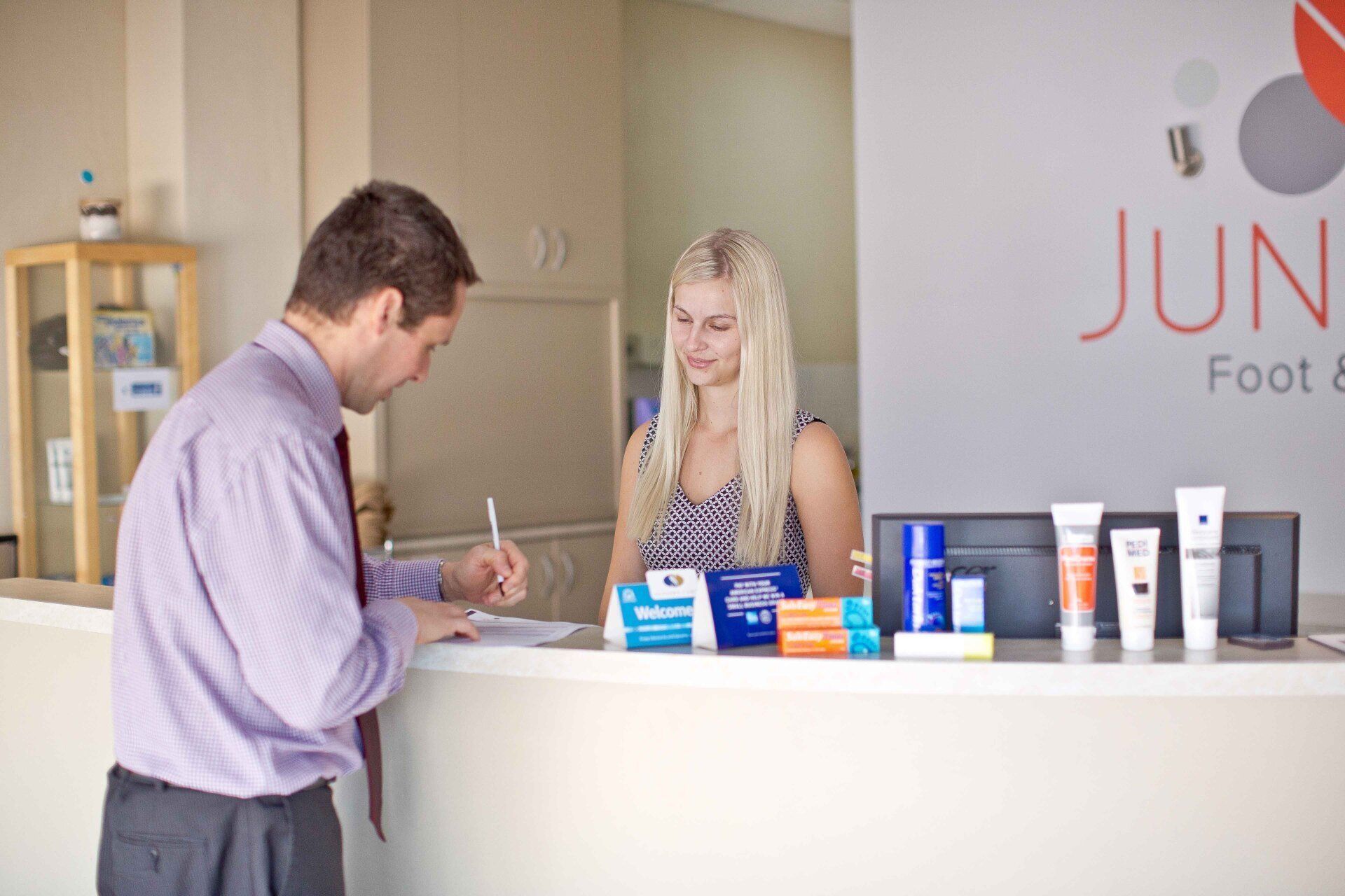 Customer at clinic counter speaking with staff beside foot care product display