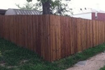 Wooden privacy fence in a yard, stained brown.
