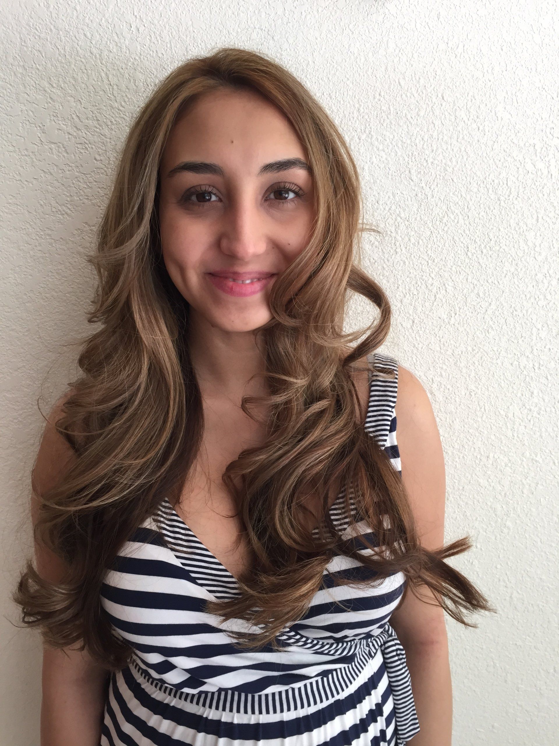 Woman with wavy brown hair, wearing a striped top, smiling in front of a white wall.