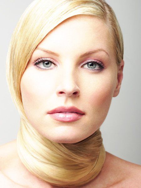 Blonde woman with light skin, hair wrapped around neck, wearing subtle pink makeup.