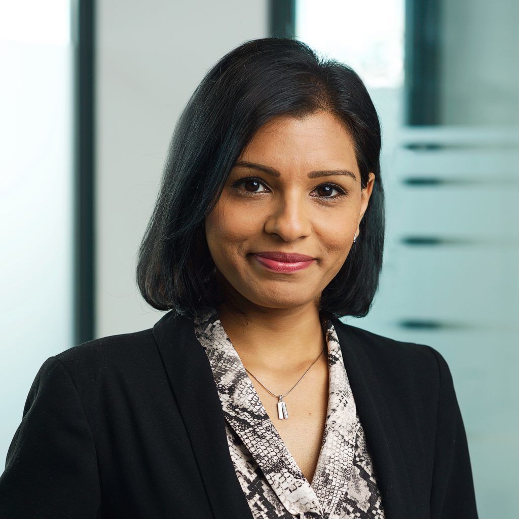 A woman wearing a black jacket and a necklace is smiling for the camera.