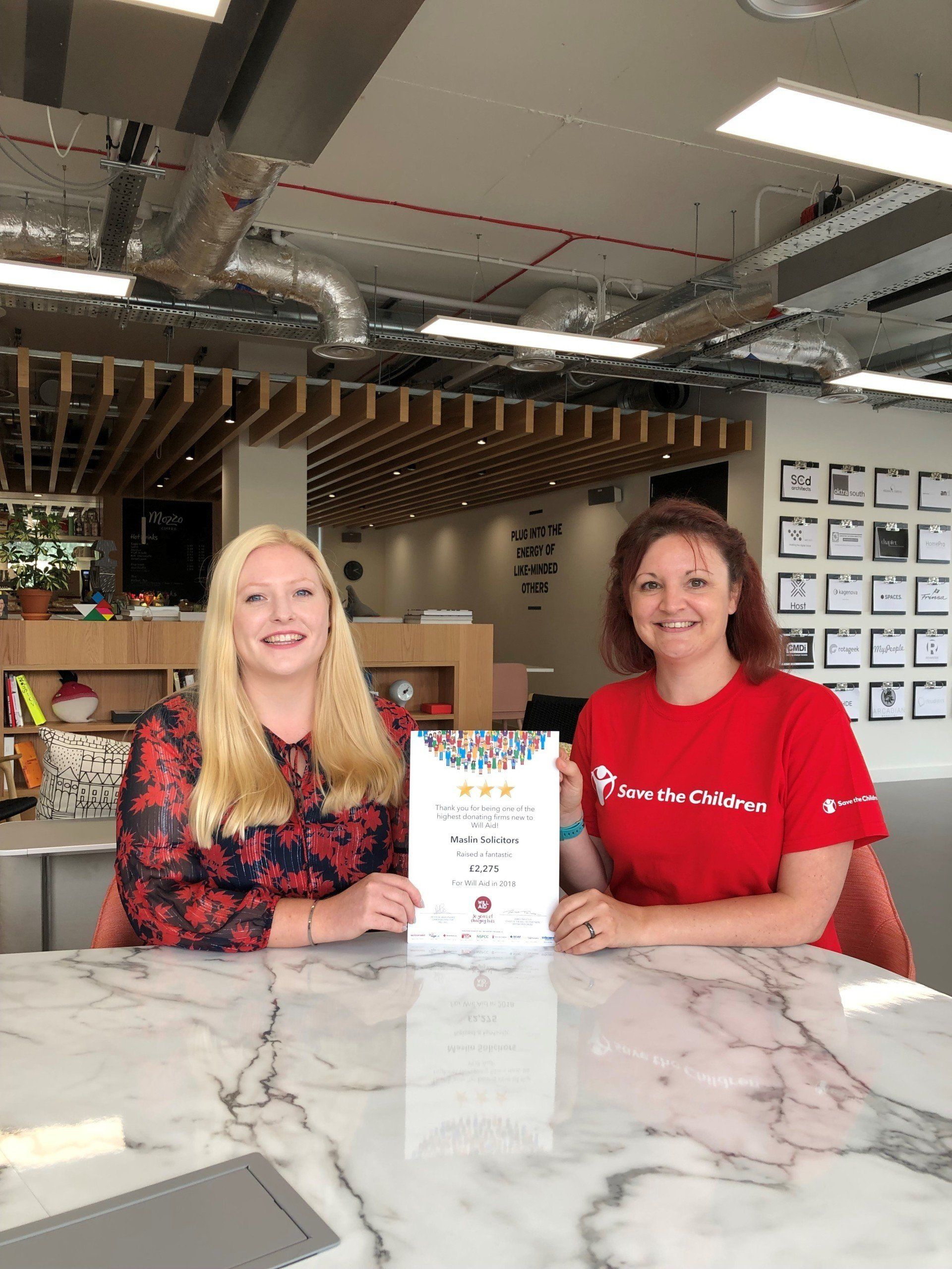 Two women are sitting at a table holding a certificate.