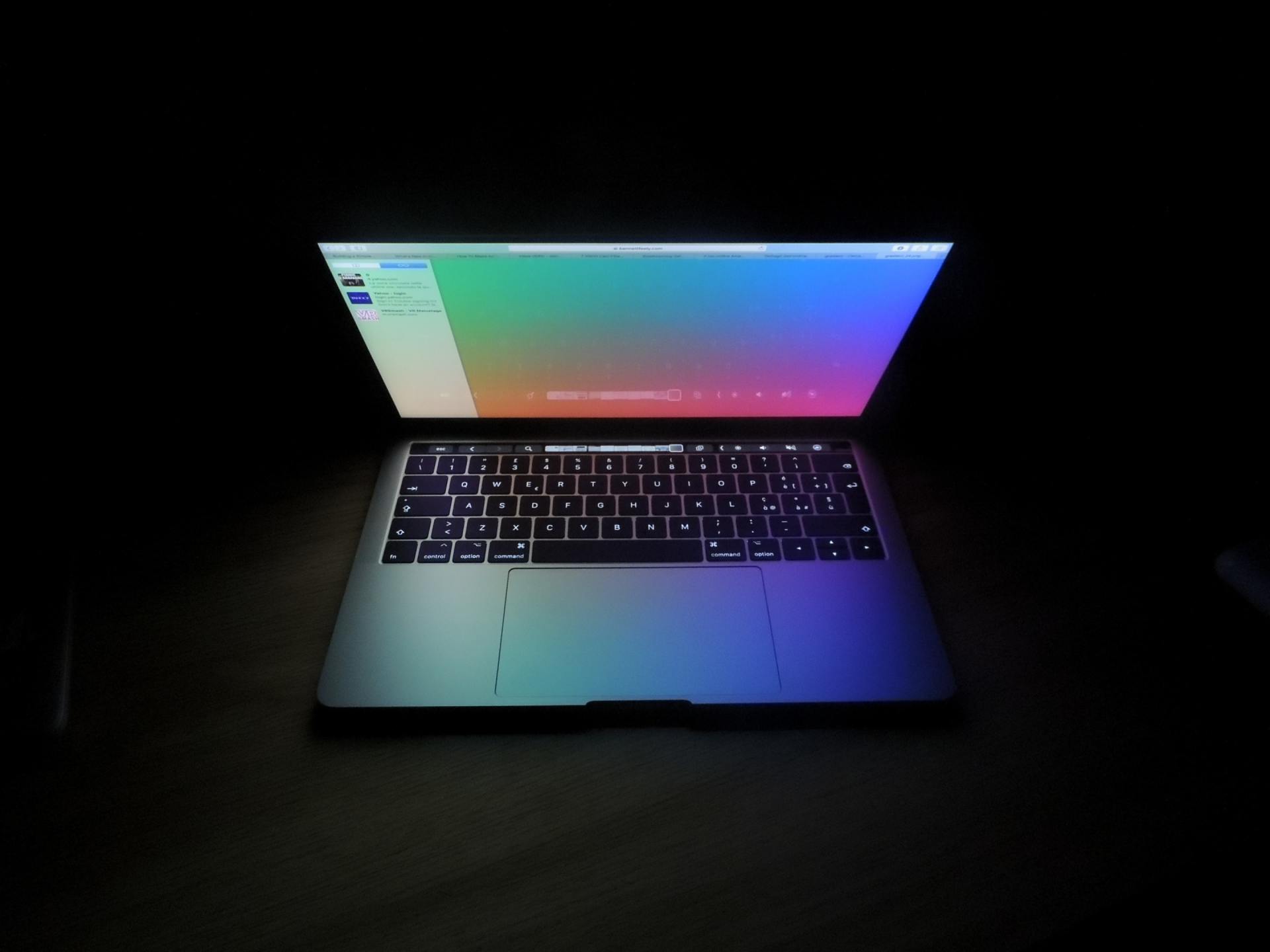 A laptop with a rainbow colored screen is open in the dark