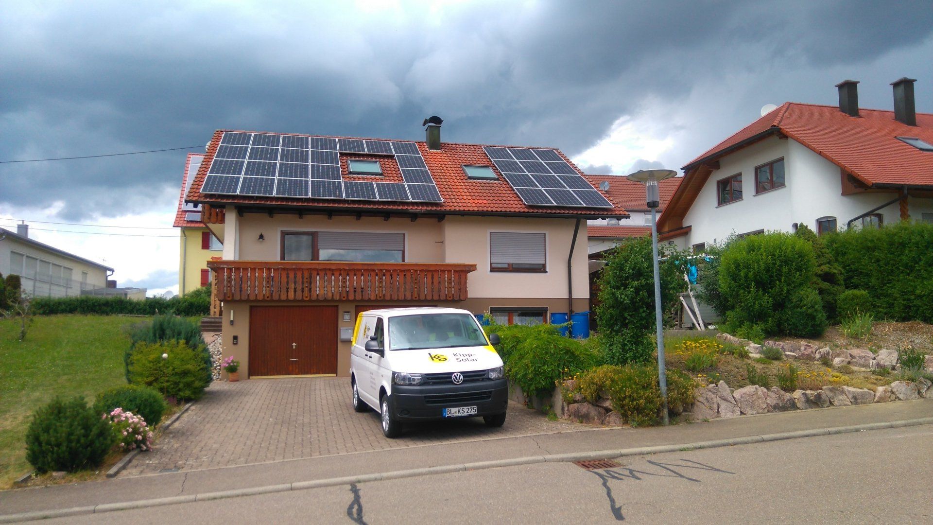 Haus mit installierten Solarmodulen, weißer Lieferwagen in der Einfahrt, bewölkter Himmel.