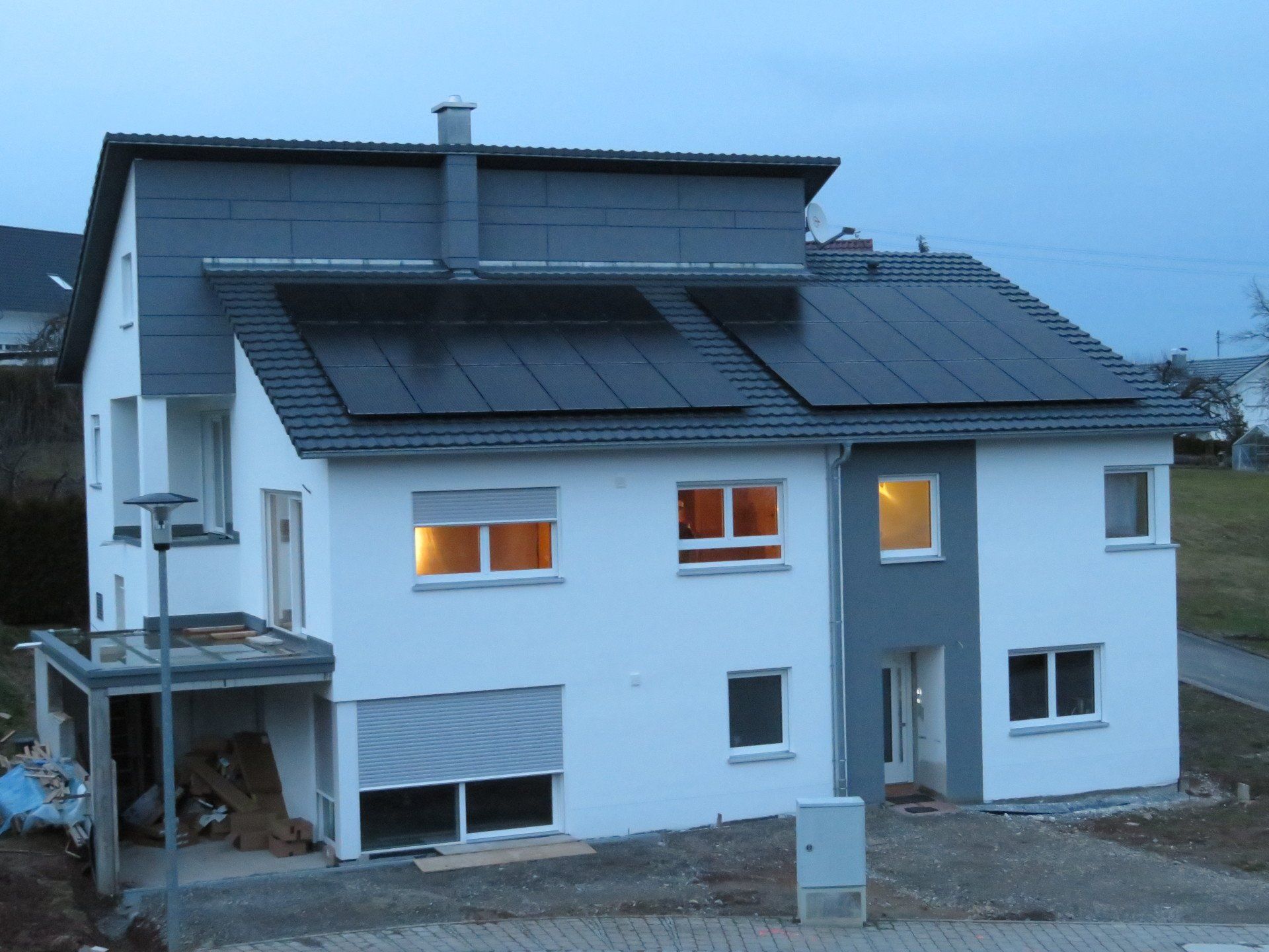 Zweistöckiges weißes Haus mit Solarzellen auf dem Dach; Innenbeleuchtung eingeschaltet. Abenddämmerung.