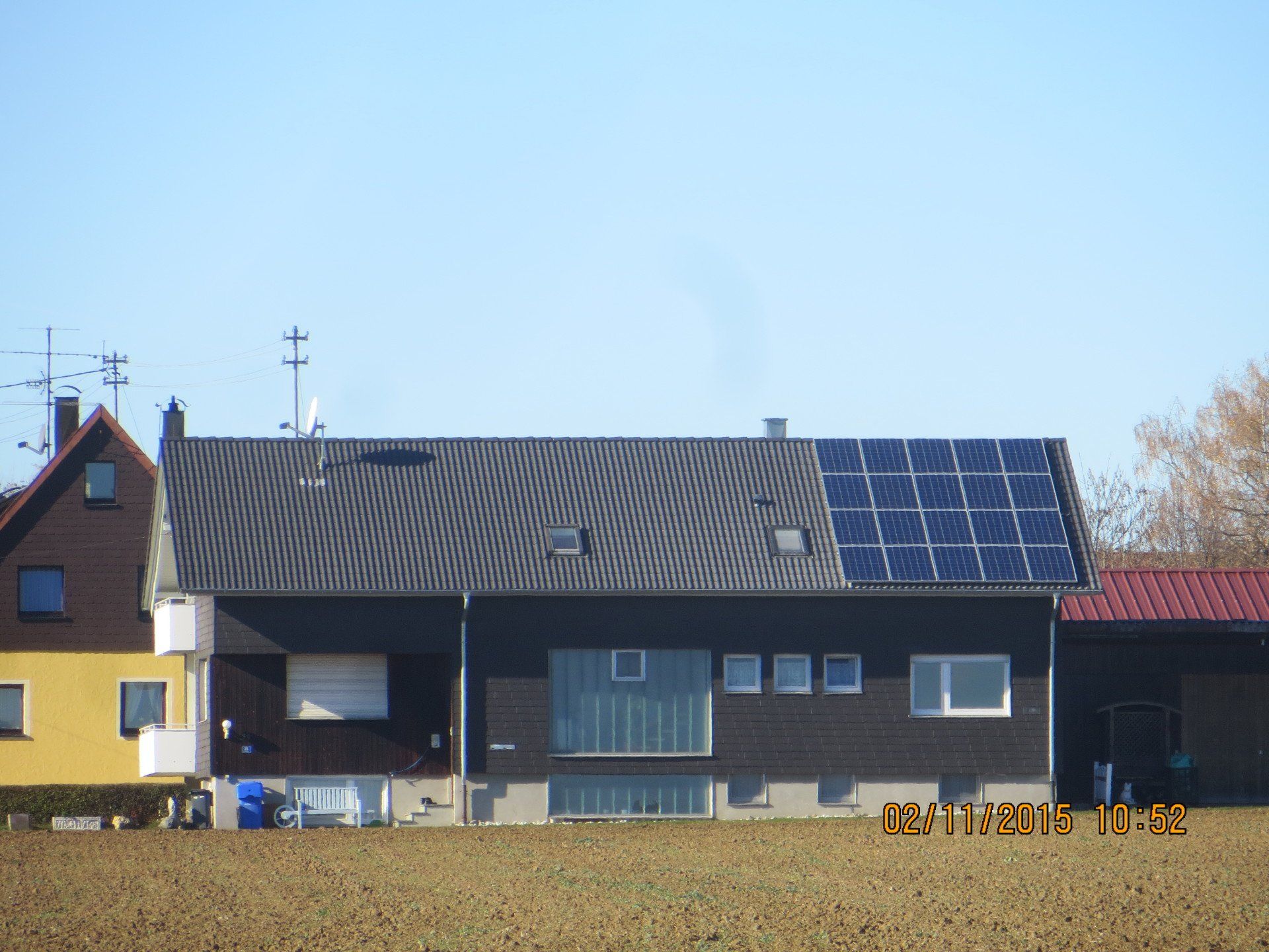 Haus mit Solarzellen auf dem Dach; dunkelgraue Außenverkleidung, mehrere Fenster, blauer Himmel.