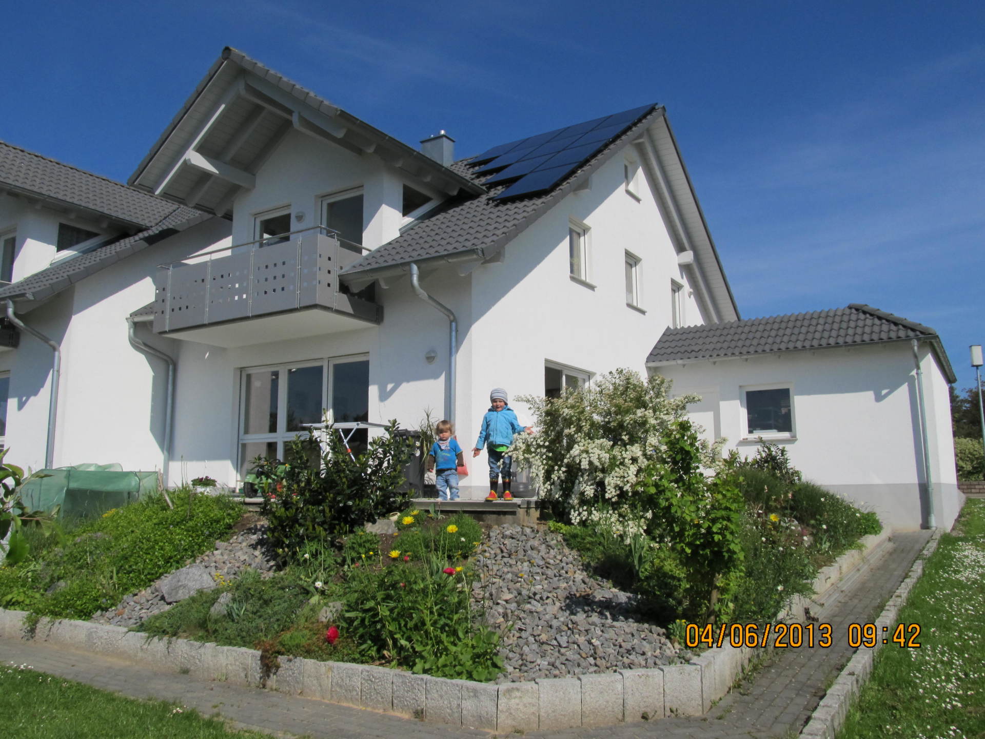 Zwei Kinder stehen auf Stufen vor einem weißen Haus mit Solarzellen auf dem Dach.