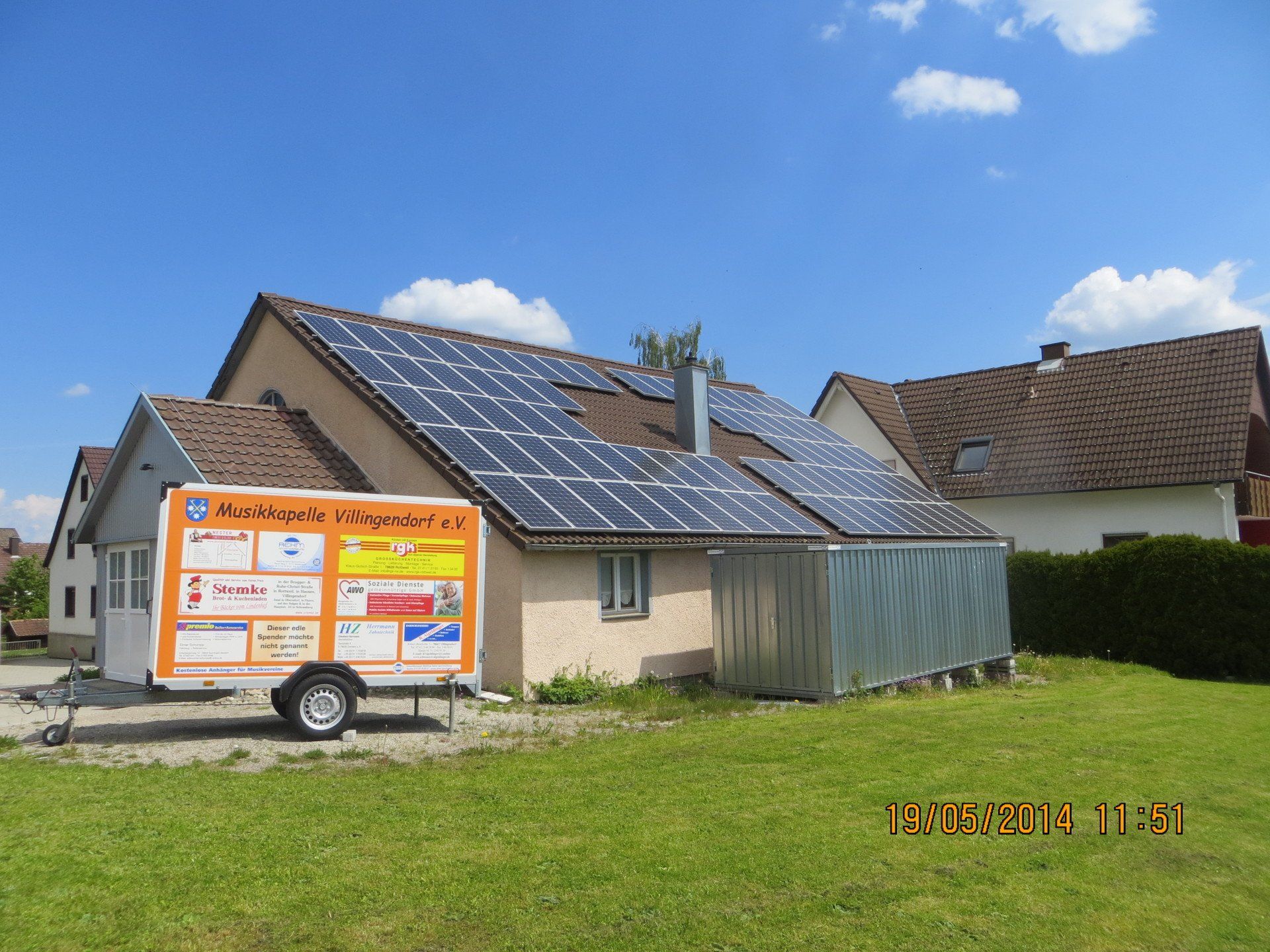 Solarmodule auf einem Haus mit einem Anhänger davor, an einem sonnigen Tag.