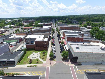 Aerial view of a small town street lined with parked cars and low buildings on a sunny day