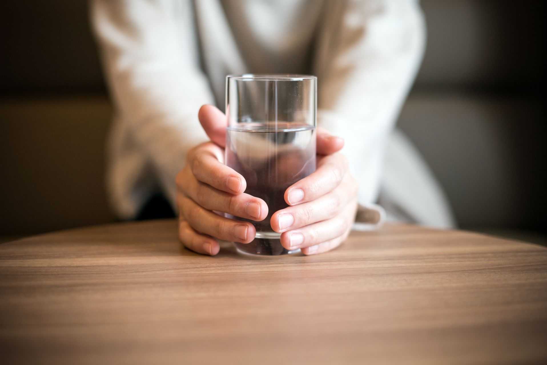 Person holding a glass of water on a wooden table; close up.