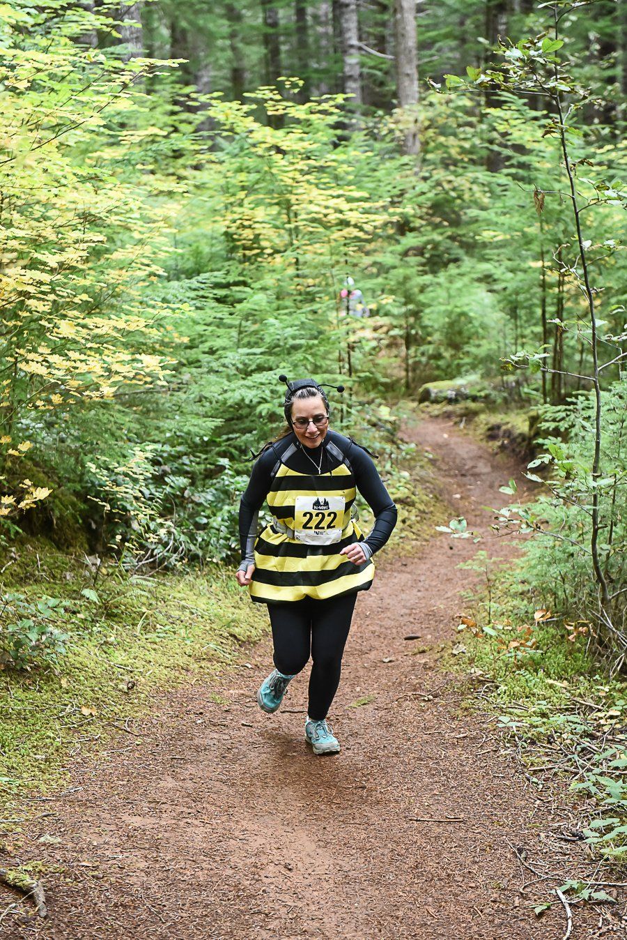 A woman in a bee costume is running down a dirt path in the woods.