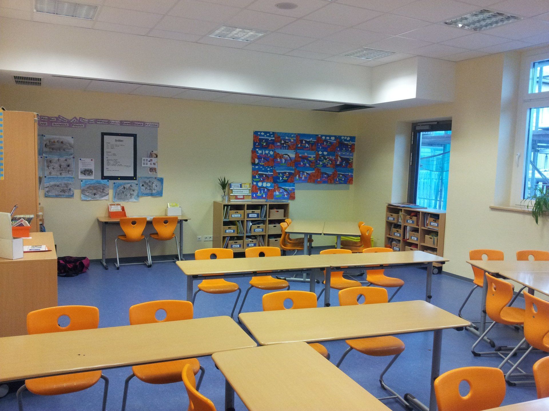 Ein hell erleuchtetes Klassenzimmer mit gelben Stühlen, Holztischen und lehrreichen Wandtafeln an cremefarbenen Wänden.