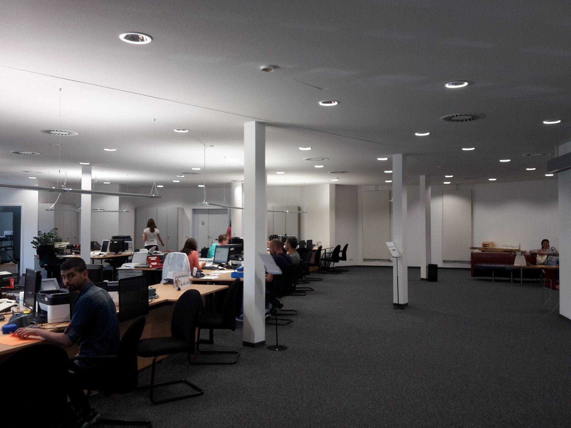 Großraumbüro mit mehreren Arbeitsplätzen, Schreibtischen, Computern und Mitarbeitern, die in einem hellen, 