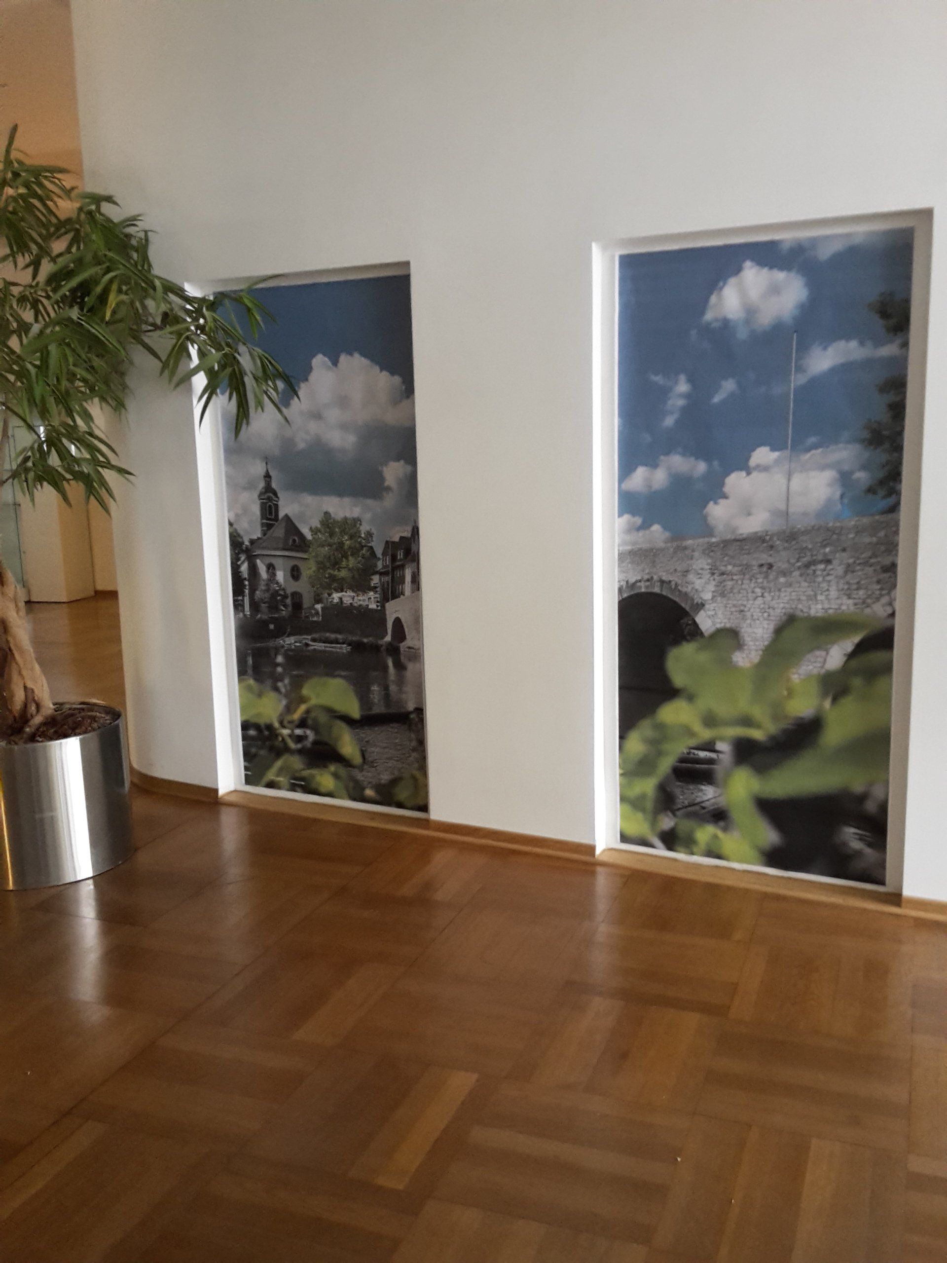 Zwei hohe, vertikale Landschaftsdrucke hingen an einer weißen Wand über einem polierten Holzboden, neben einer Topfpflanze.