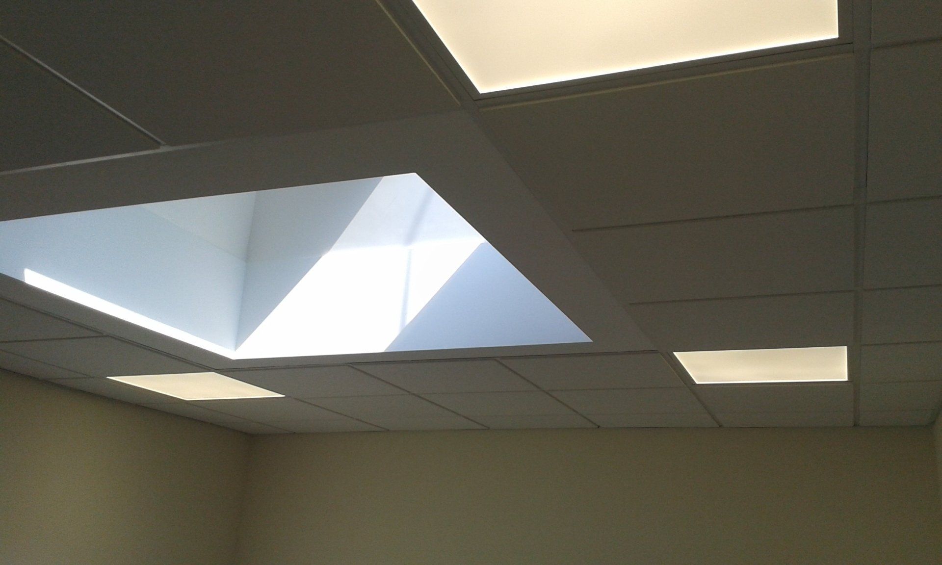 Eine abgehängte Decke mit einem eingelassenen quadratischen Oberlicht und zwei bündig montierten weißen LED-Lichtpaneelen.