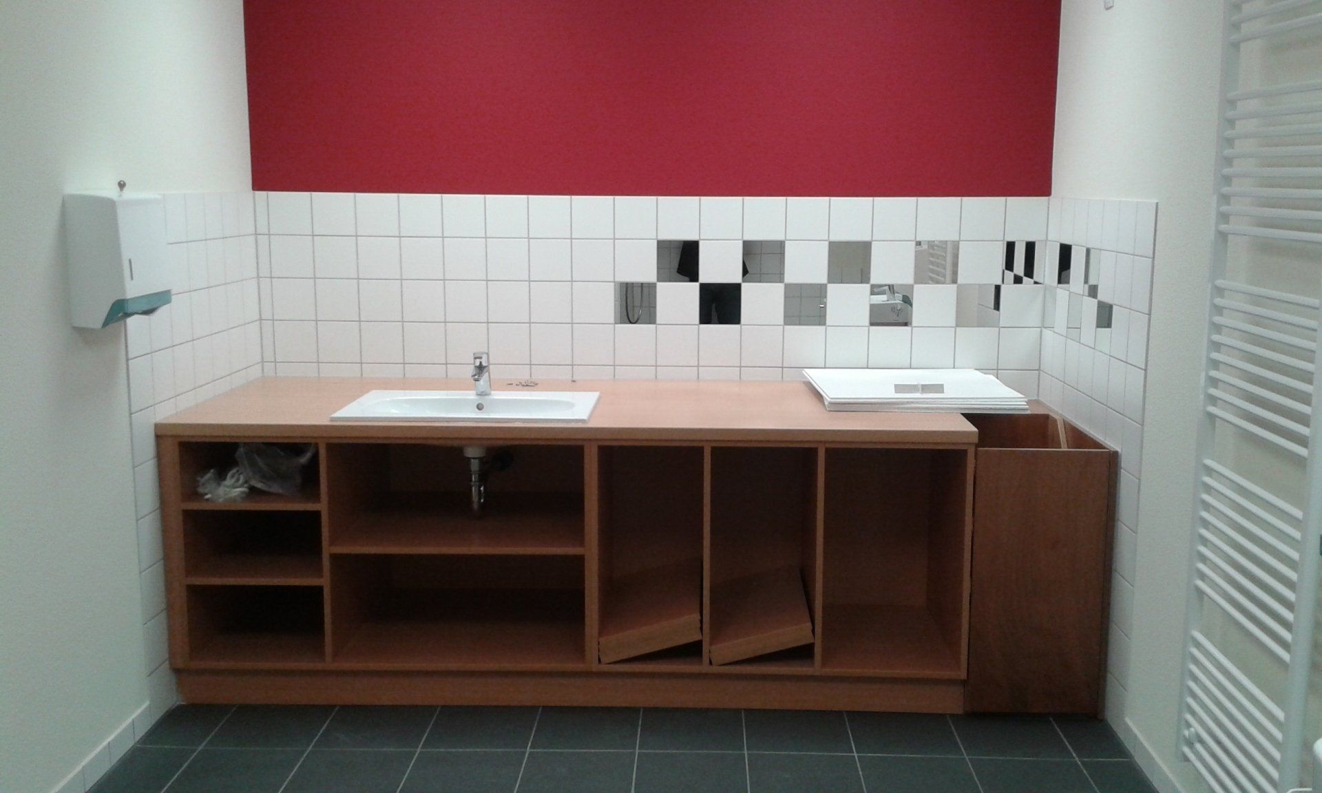 Ein Badezimmerschrank mit Waschbecken aus Holz, einem weißen Becken, weiß gefliesten Wänden