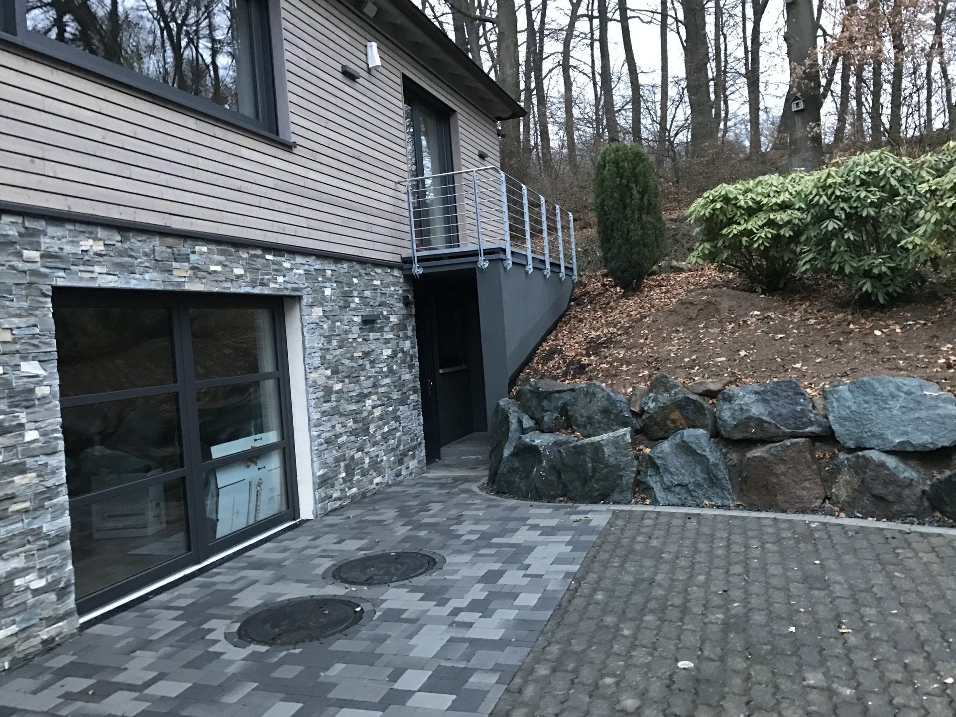 Ein modernes Hausäußeres mit einem steinverkleideten Kellergeschoss, einer gepflasterten Terrasse und einem 