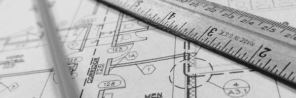 Eine Schwarz-Weiß-Nahaufnahme eines Metalllineals, das auf detaillierten architektonischen Grundrisszeichnungen liegt.