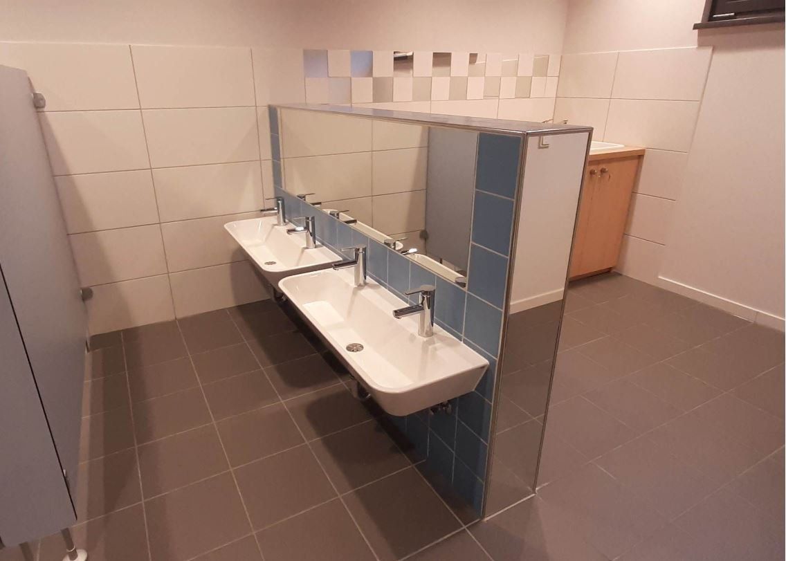 Zwei weiße, rechteckige Waschbecken mit verchromten Armaturen sind an einer blau gefliesten Trennwand in einem Badezimmer