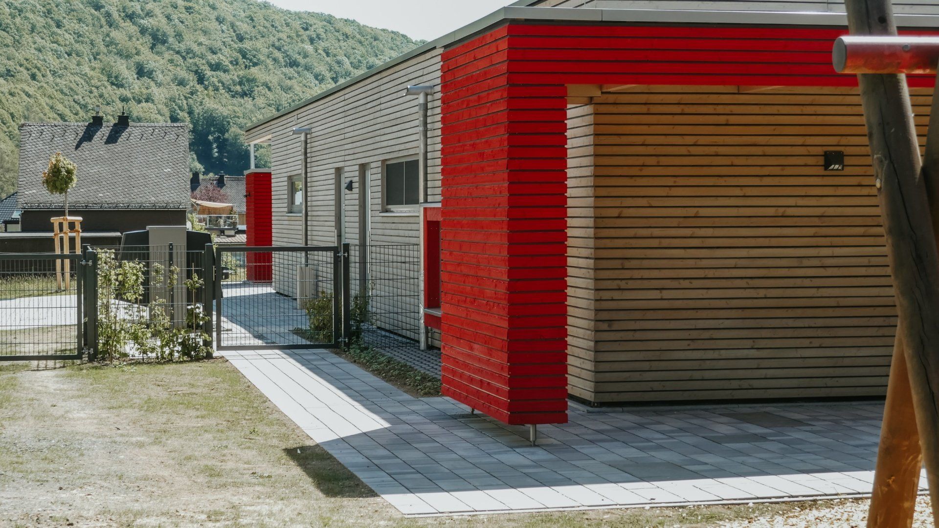 Ein modernes Haus mit horizontaler Holzverkleidung und leuchtend roten Akzenten, gepflastertem Weg