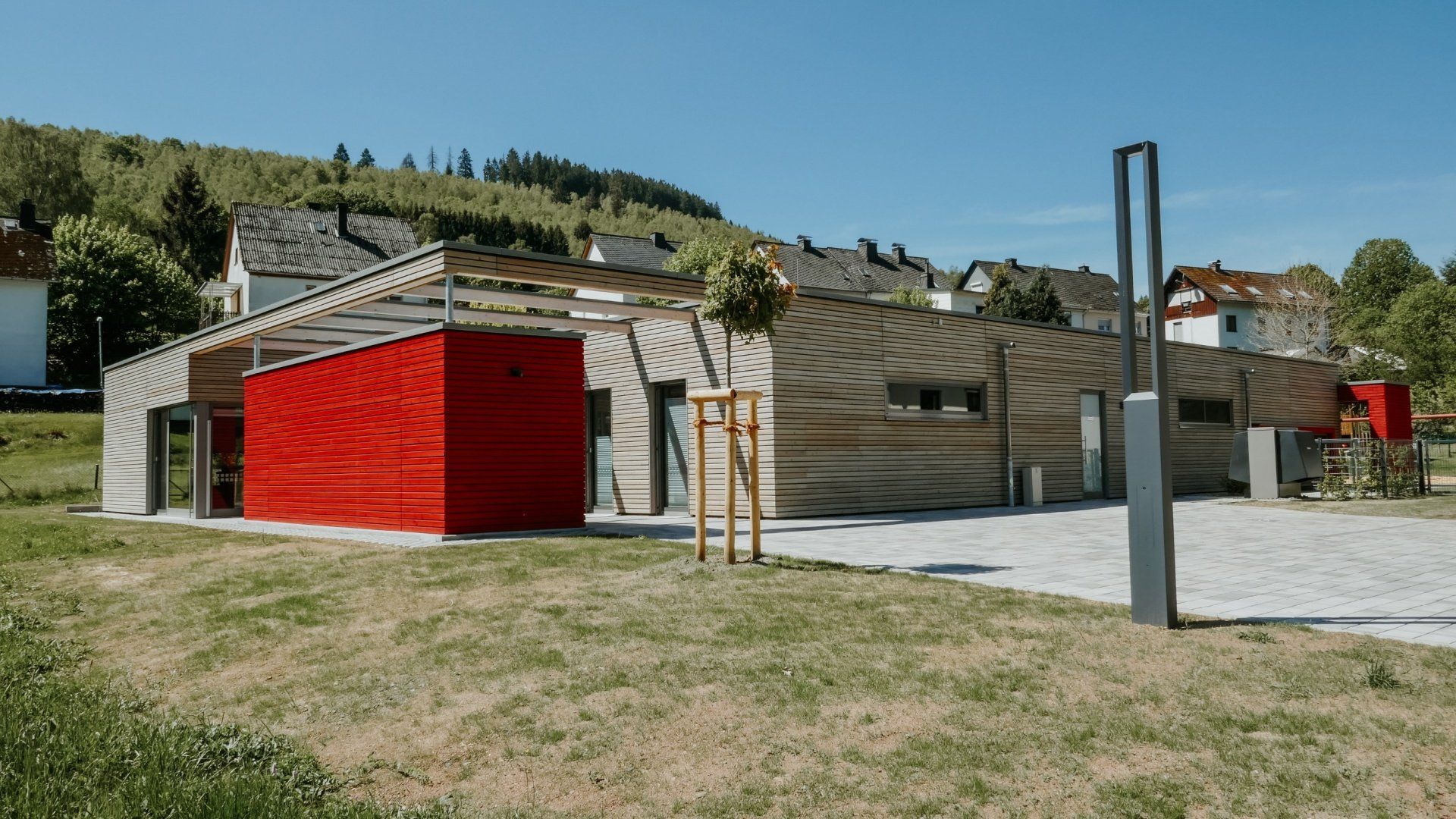 Ein eingeschossiges, holzverkleidetes modernes Gebäude mit einem markanten leuchtend roten Abschnitt und einem schrägen Dach,