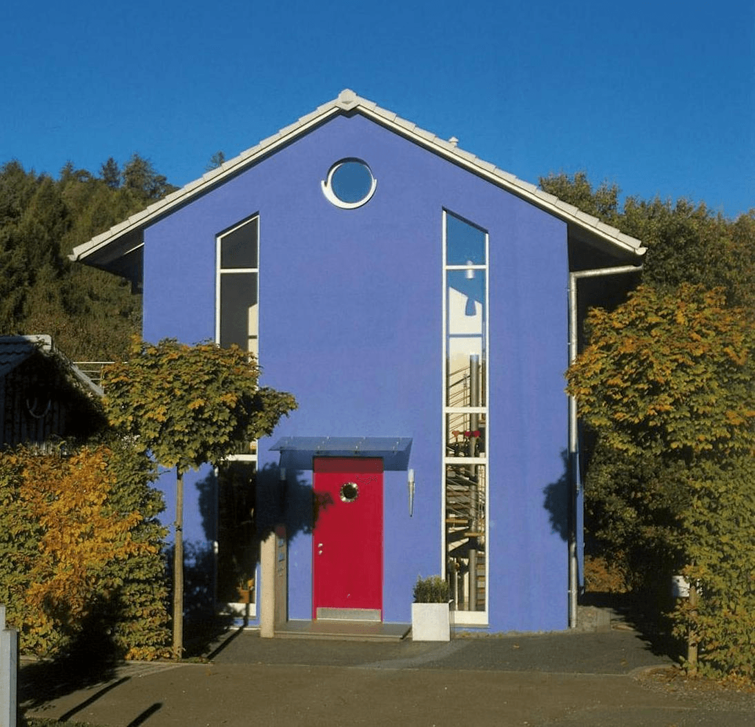 Ein blaues zweistöckiges Haus mit einer leuchtend roten Eingangstür, hohen, vertikalen Fenstern und einem kleinen