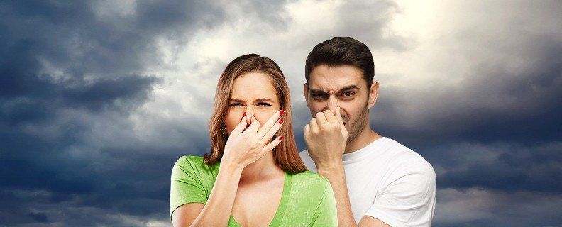 A woman and a man pinch their noses, expressing disgust. Cloudy sky background.