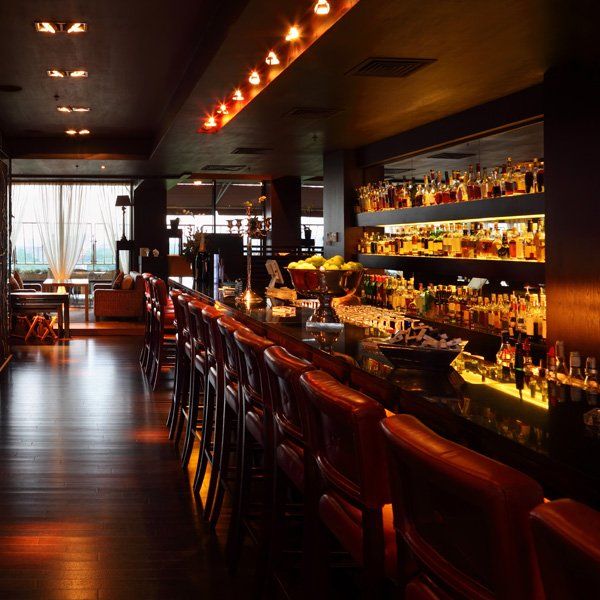 Dark bar interior with red leather chairs, extensive liquor selection, and warm lighting.