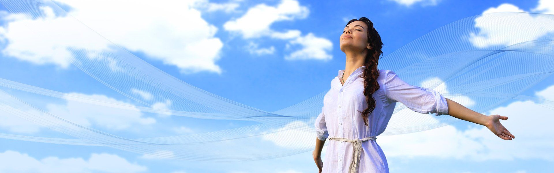 Woman with arms outstretched, looking upward at a blue sky with clouds.
