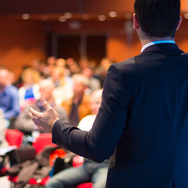 Man in suit giving a presentation to an audience in a conference room.