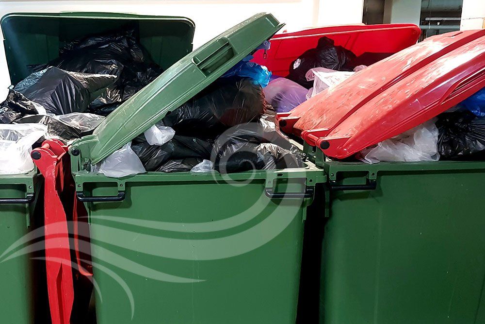 Green and red overflowing trash bins, black bags of garbage, lid slightly open.