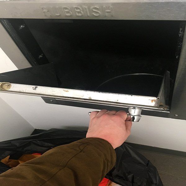 Hand opening a metallic rubbish bin. The word