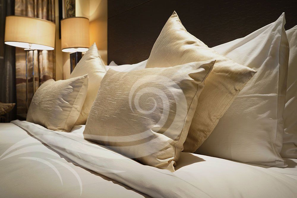 Bed with a stack of cream-colored pillows, lit by lamps in a dimly lit room.