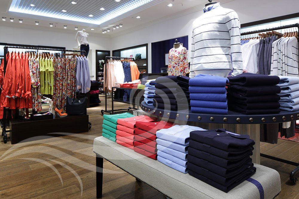 Clothing store interior with stacked and hanging apparel; bright lights.