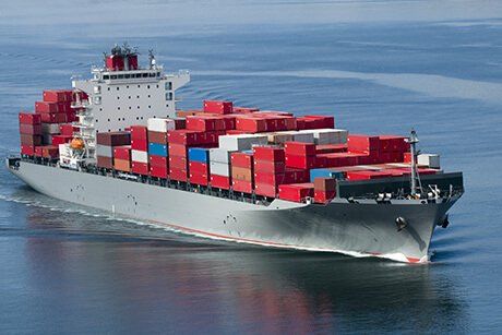 Container ship sailing on calm blue water, carrying stacks of colorful cargo containers.