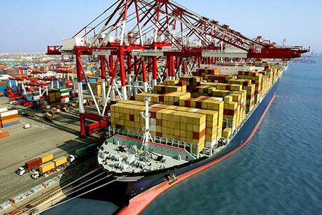 Large cargo ship docked at a port, being loaded and unloaded by large red cranes.