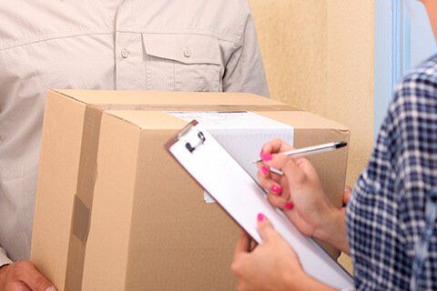 Person signing clipboard, receiving package from delivery person.