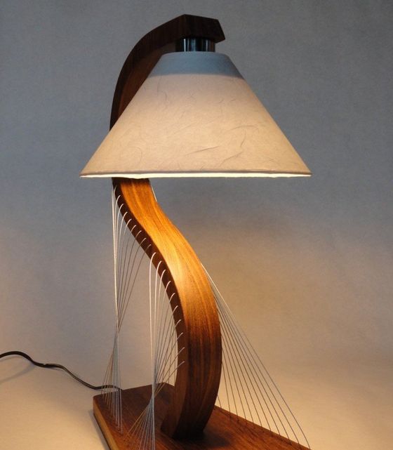 Modern sculptural table lamp with a cream shade, curved wooden base, and thread-like side accents