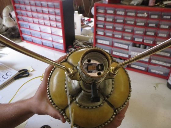 Handheld close-up of a brass mechanical device with two long arms and red parts on a workbench