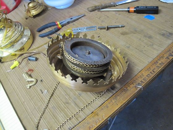 Disassembled metal lamp parts on a wooden workbench with tools and a ruler nearby