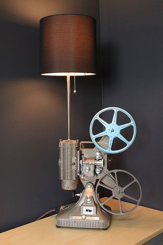 Vintage film projector lamp with a black shade on a wooden table against a dark wall